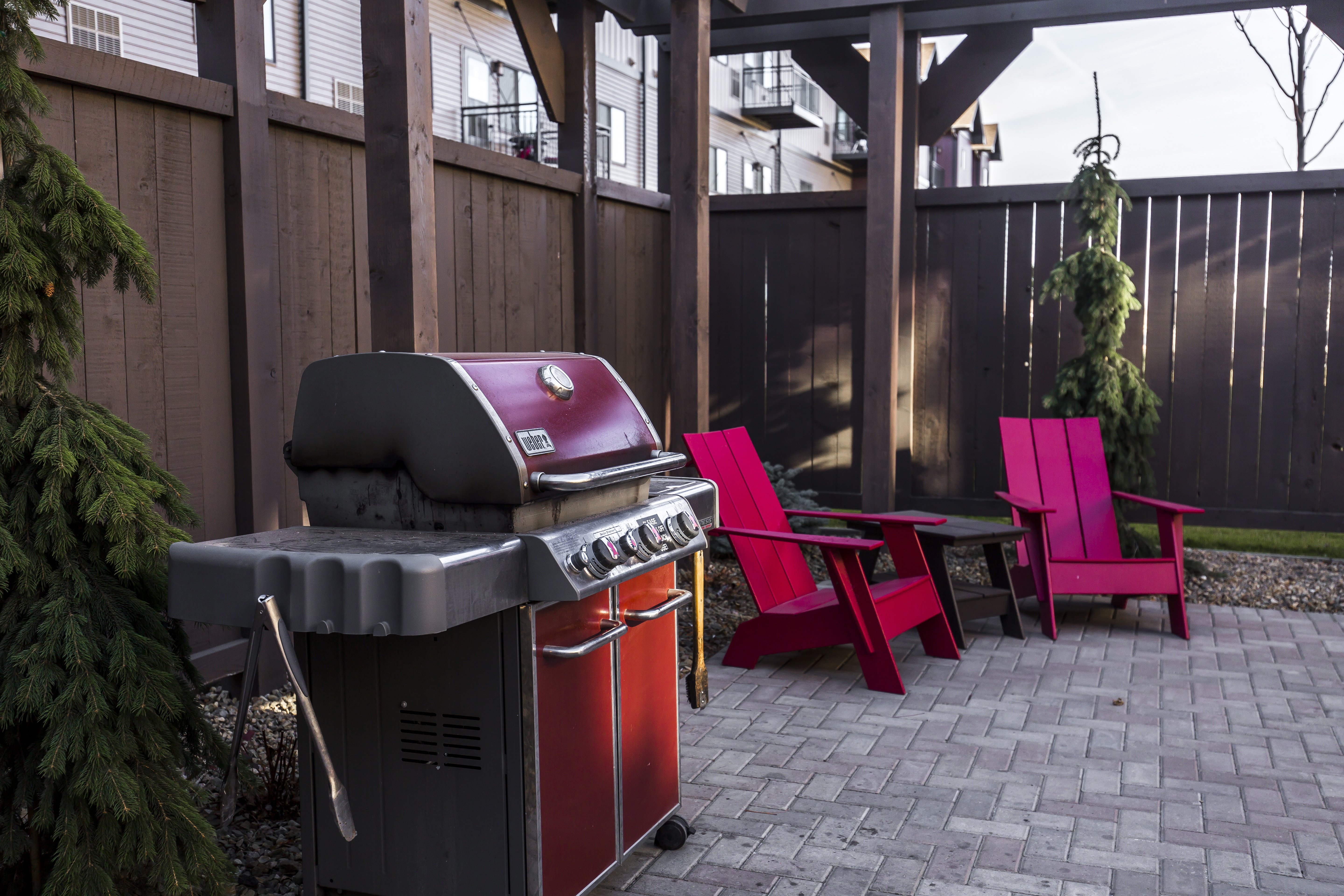 A red grill is in the middle of a patio with matching red chairs.